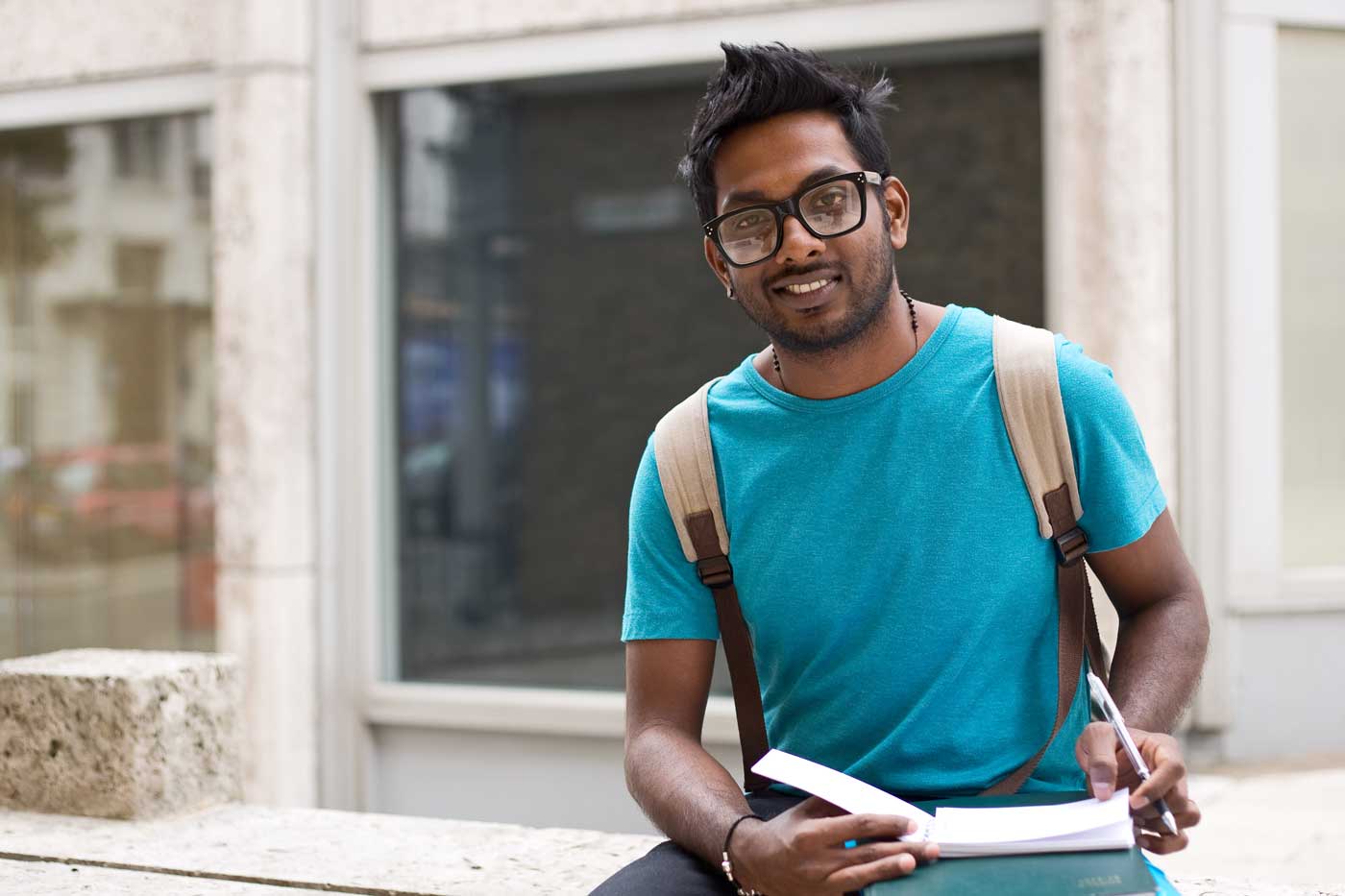 male-student-with-glasses-backpack-books-in-blue-shirt